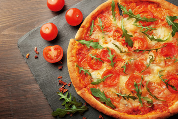 Margherita pizza with tomatoes and arugula on slate plate