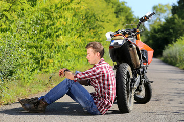 young man sitting on the road in addition the motorcycle