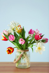 Bouquet of beautiful colorful tulips on wooden table against light blue wall background