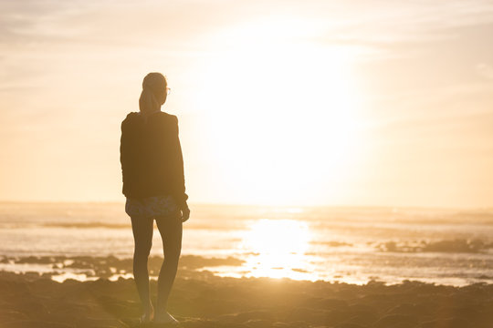 Silhouette of meditative, sensual blonde woman watching sunset at the beach.
