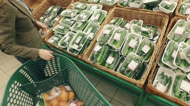Woman buy fresh cucumbers in modern supermarket