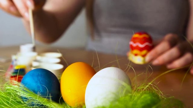 Preparing for a happy Easter.A young Woman Paints Easter Egg with a Brush on the background of Wooden Table.by refocusing