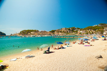 Fototapeta na wymiar Colorful umbrellas on Puerto de Soller, Port of Mallorca island in balearic islands, Spain. Beautiful picture of people resting on the beach on bright summer day.