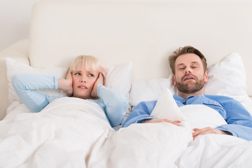 Woman Covering Ears While Man Snoring In Bed