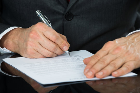 Close-up Of Businessman Hand Holding Pen Over Contract Form