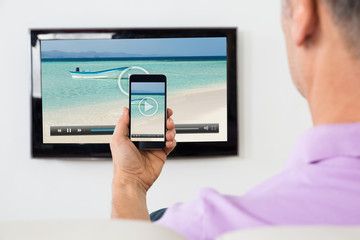 Man With Smartphone Connected To A TV Watching Video