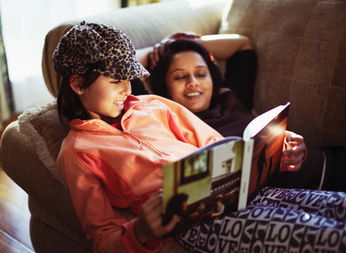 Mother and daughter reading book on sofa