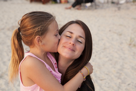 Caucasian girl kissing cheek of mother on beach