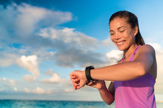 Active girl using fitness tracker smart watch jogging on summer nature outdoors looking at health data during sports activity touching the screen of her smartwatch.