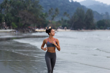 Young slim woman running barefoot on the ocean beach at sunset