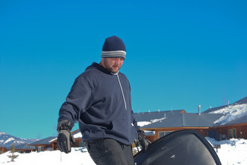 Man in toboggan carrying a snow sled.