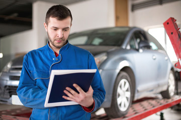 Mechanic in auto repair shop standing and writing on clipboard - 106846013