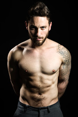 Fototapeta premium Handsome young man with tattoos posing. Isolated on black.
