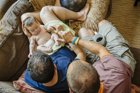 Caucasian Gay Couple Holding Sleeping Baby Boy On Sofa