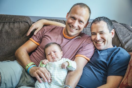 Caucasian gay couple smiling with baby boy on sofa