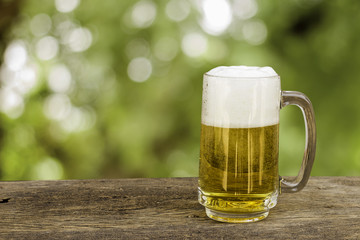 Beer in glass on wooden table with blurred green summer leaves o