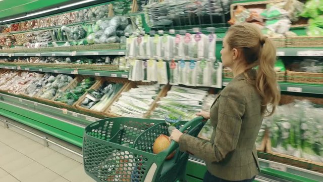 Young blond woman walk along shelves with greenery in supermarket