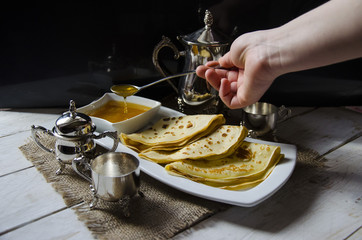 Yeast pancakes traditional for Russian pancake week witn honey on white plate black background