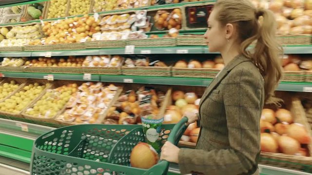 Young blond woman walk along shelves with fruits in supermarket