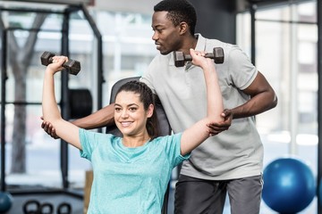 Athletic woman lifting weights helped by trainer