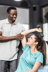 Fototapeta premium Athletic woman lifting weights helped by trainer