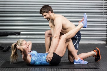 Obraz premium Male trainer assisting woman with sit ups