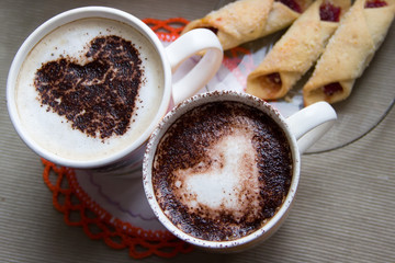 Two cups of coffee with a heart painted on the surface and cooki