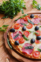 Pizza with salami, black olives and tomatoes on the wooden table.
