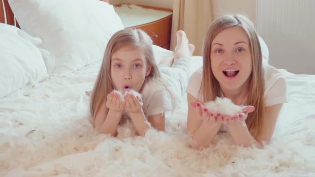 Cute girls lying on the bed and playing with fluff and feathers. Slowmotion