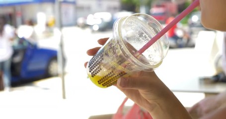 Closeup shot of a plastic cup with lid in human hand. Person is drinking juice or non-alcohol cocktail through the straw.
