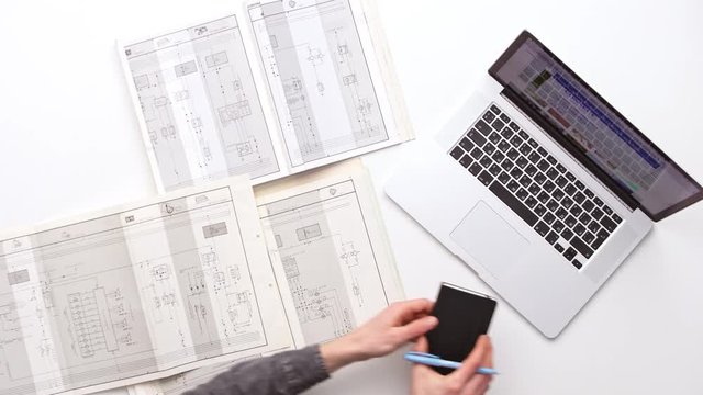 Man working at office desk with his laptop surrounded by a lot of plans. Upview