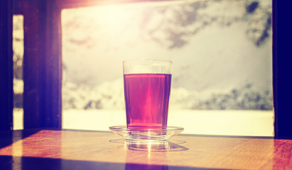 Retro old film style glass of hot tea on wooden table by a mountain shelter window, coziness and comfort concept, shallow depth of field.
