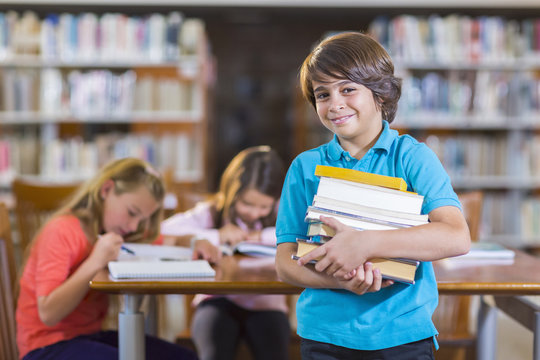 Student carrying stack of books in library - Powered by Adobe