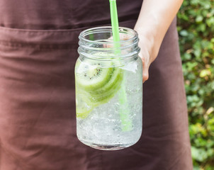 Hand on serving glass of iced kiwi soda drink
