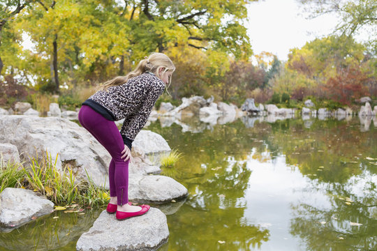 Caucasian girl crouching on rock in pond