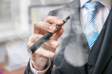 Businessman holds vaporizer and is smoking electronic cigarette.