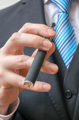 Businessman in suit holds vaporizer in hand.