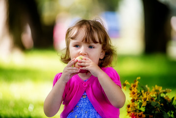 Fototapeta premium Cute little girl eating apple in the park