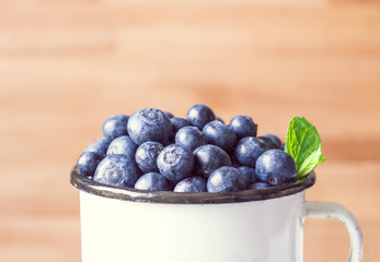 Detail of fresh blueberries with green mint leaves in tinny cup on wood