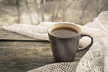Cup of black coffee in front of the window and a lace on the wooden background.