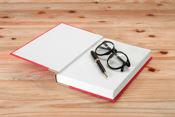 red book with glasses and pen on the wooden