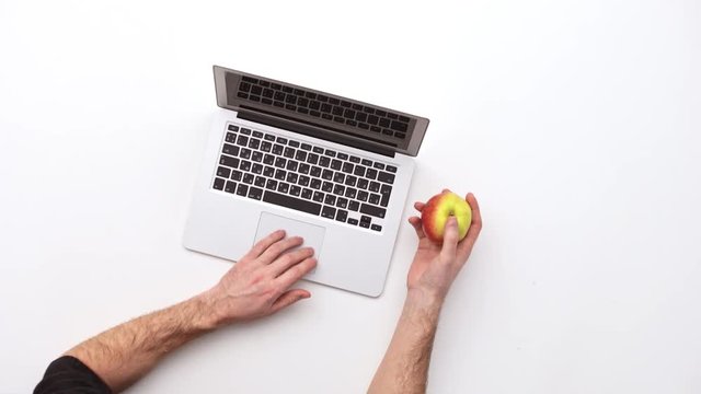 Man types on a laptop on his desk with apple.  Upview