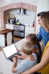 Fototapeta na wymiar Parents and kids using laptop in kitchen