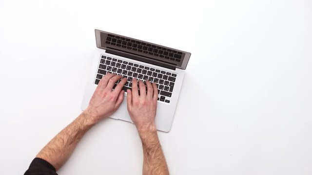 Man types on a laptop on his desk. Upview