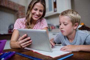 Mother using a digital tablet while helping son with his homework