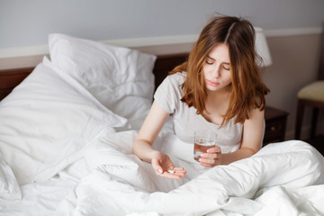 Sick woman looking on pills in her hand