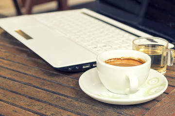 vintage color tone, laptop and cup of coffee on the table coffee shop [blur and select focus background]