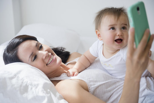 Mixed race mother playing with baby and cell phone on bed