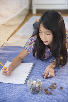 Vietnamese girl counting coins on bedroom floor