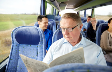 happy senior man reading newspaper in travel bus